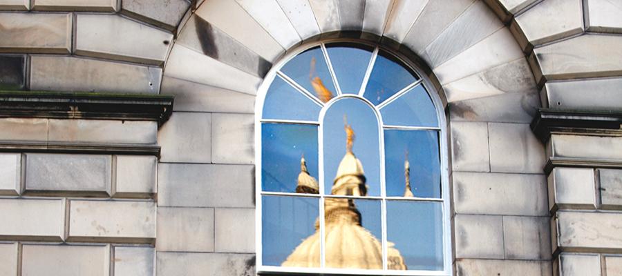 Reflection of golden statue of Old College in window pane