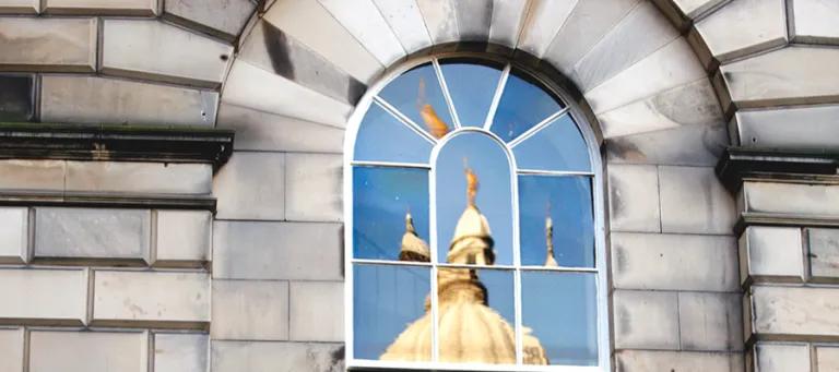 Reflection of golden statue of Old College in window pane